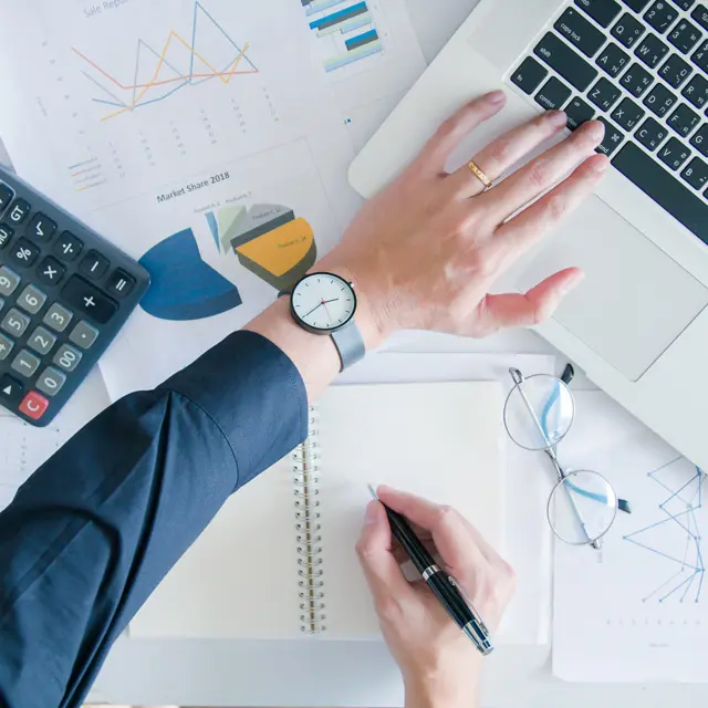 Hand on a desk with a laptop, calculator and documents Hand on a desk with a laptop, calculator and documents