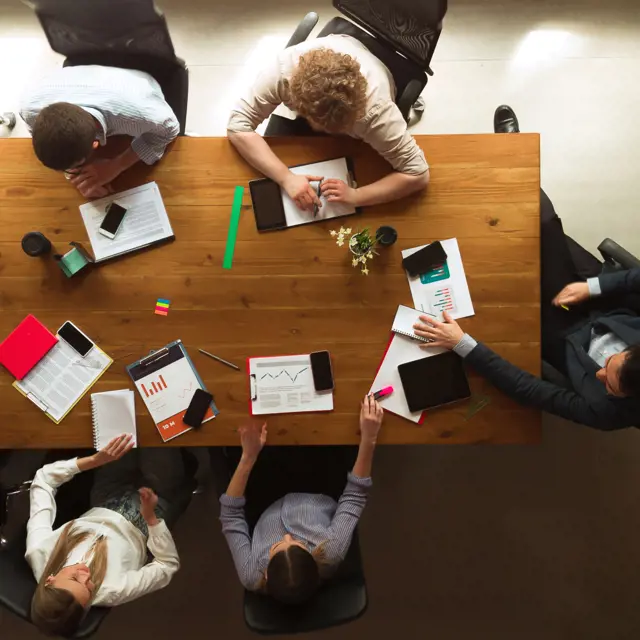 People working around a wooden table together and looking at data People working around a wooden table together and looking at data